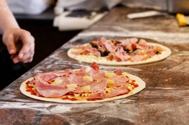 Aşçı iki pizzaya malzeme koyuyor..