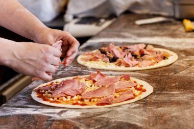 Aşçı iki pizzaya malzeme koyuyor..