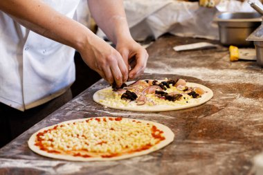 Aşçı iki pizzaya malzeme koyuyor..