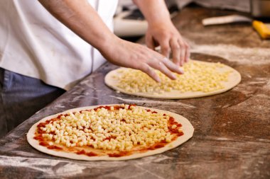 Aşçı iki pizzaya malzeme koyuyor..