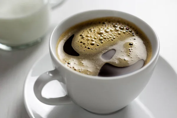 Freshly poured black coffee with froth in white ceramic cup next — Stock Photo, Image