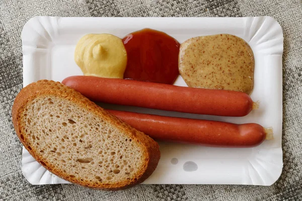 Een paar worstjes frankfurter met een sneetje brood op papieren plateau — Stockfoto