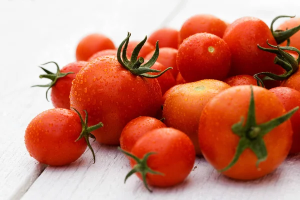 Tomates mixtos húmedos grandes y pequeños con tallos en boa de madera blanca — Foto de Stock