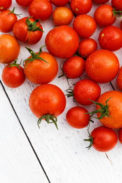 Beaucoup de tomates rouges humides avec des tiges sur panneau de bois blanc d'en haut — Photo