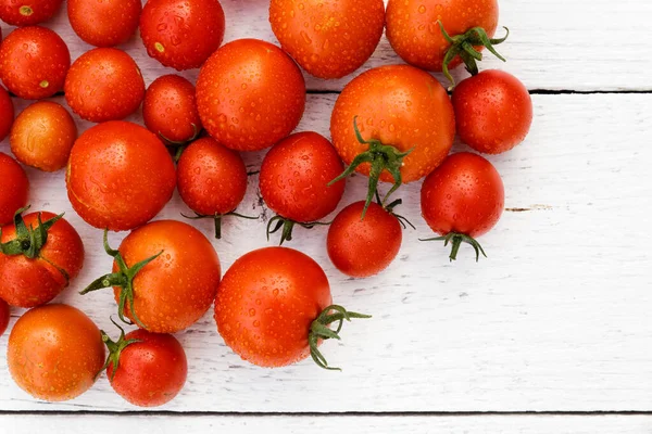 Beaucoup de tomates rouges humides avec des tiges sur panneau de bois blanc d'en haut — Photo