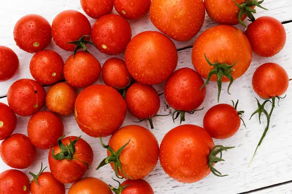 Many wet red  tomatoes with stalks on white wood board from abov — Stock Photo, Image