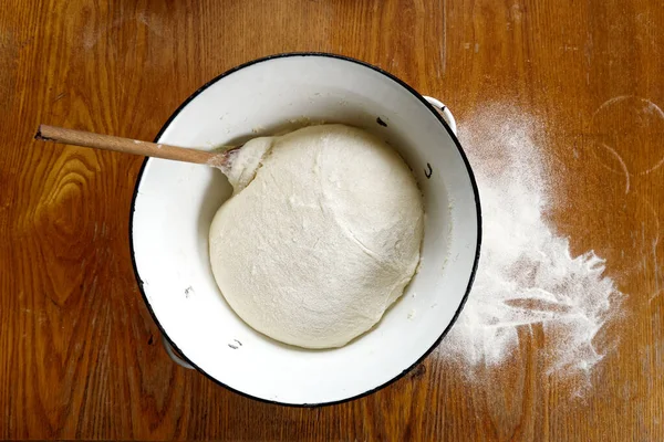 Растущее дрожжевое тесто с деревянной ложкой в металлической чаше из белой эмали — стоковое фото