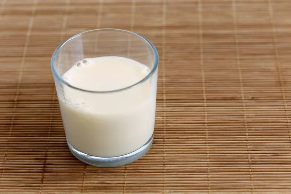 Bicchiere di latte di soia con schiuma su tappetino di bambù. Spazio per testo . — Foto Stock