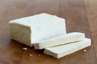 Bir kalıp beyaz tofu ve tahta doğrama tahtasındaki iki tofu dilimi.