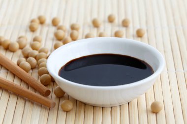 Soya sosu beyaz kasede bambu hasırı üzerinde yemek çubuklarıyla ve döküldü.