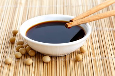Soya sosu beyaz kâse içinde bambu hasırı üzerinde yemek çubukları dinleniyor.