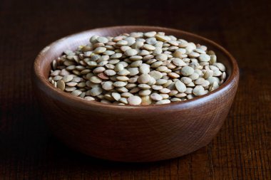 Kahverengi ahşap kasede koyu yeşil mercimek..