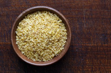 Kahverengi ahşap kasede kuru bulgur buğdayı.