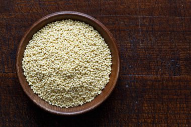 Kahverengi ahşap kasedeki kuru darı yukarıdan izole edilmiş koyu ahşap.