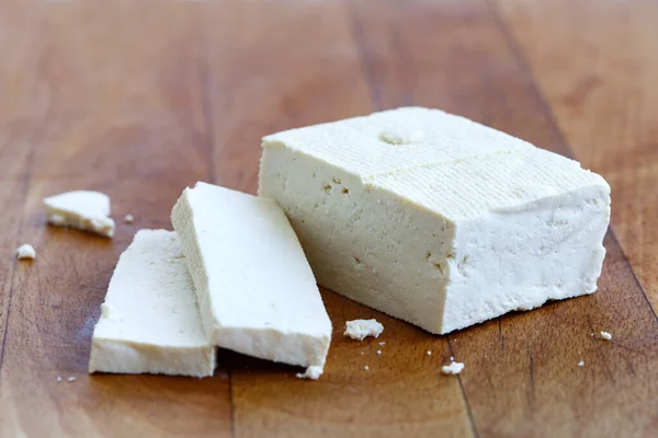 Ein Block weißer Tofu und zwei Tofu-Scheiben mit Krümeln auf dem Tisch — Stockfoto