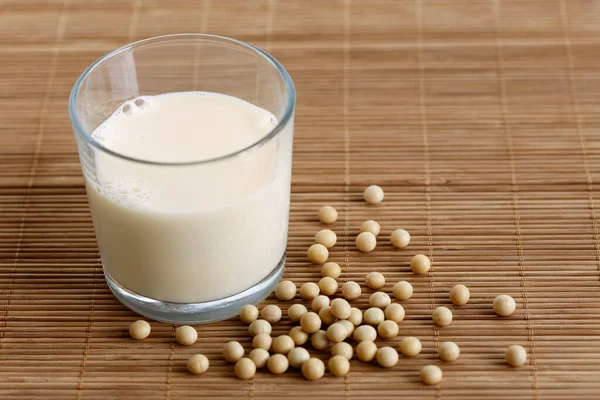 Vaso de leche de soja con espuma en estera de bambú con soja derramada —  Fotos de Stock