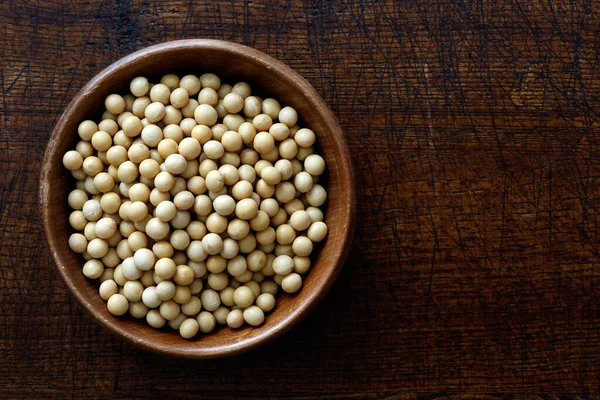 Dry soya beans in dark wooden bowl isolated on dark brown wood f — Stock Photo, Image