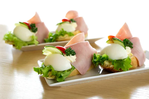 Sandwiches europeos tradicionales de huevo abierto y jamón sobre ceramica blanca —  Fotos de Stock