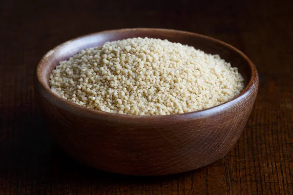 Couscous seco en cuenco de madera marrón aislado en madera oscura . —  Fotos de Stock