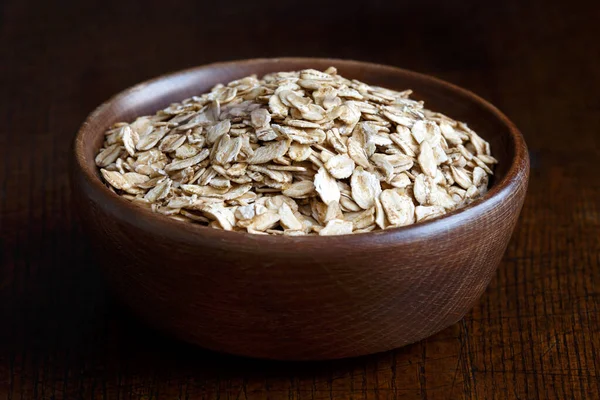 Dry porridge oats in brown wooden bowl isolated on dark wood. — Stock Photo, Image