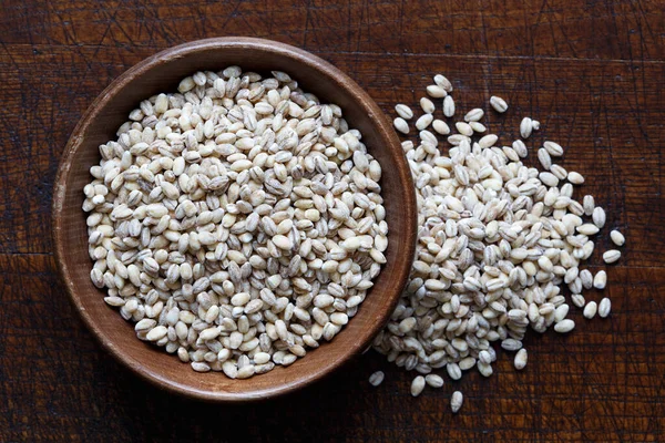 Dry pearl barley in brown wooden bowl isolated on dark wood from