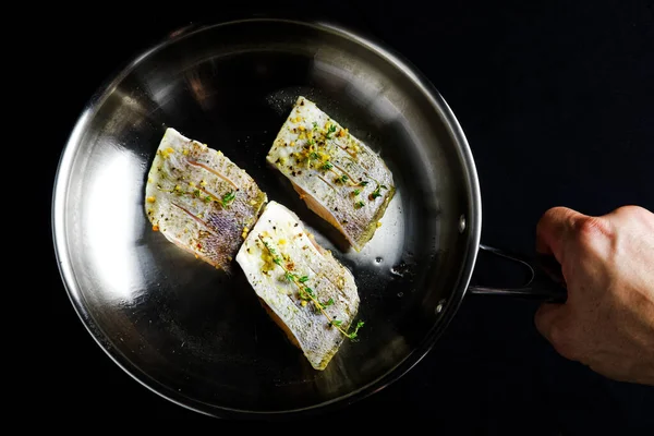 Una mano sosteniendo tres filetes de pescado con hierbas y especias en una sartén —  Fotos de Stock