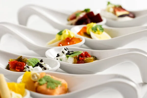 Una fila di tartine miste in cucchiai di ceramica bianca su dorso bianco — Foto Stock