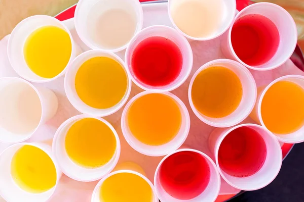Mix of children drinks in white plastic cups from above. — Stock Photo, Image