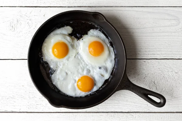 Три жареных яйца в чугунной сковороде изолированы на белой краске — стоковое фото