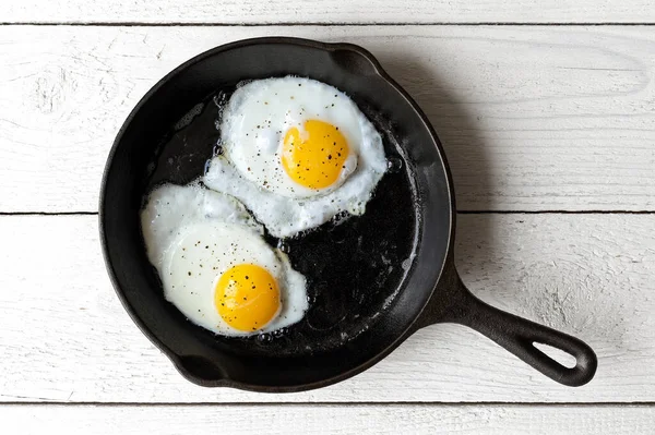Dos huevos fritos en sartén de hierro fundido espolvoreados con bla molida —  Fotos de Stock