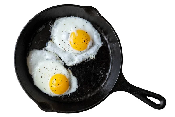 Dos huevos fritos en sartén de hierro fundido espolvoreados con bla molida —  Fotos de Stock