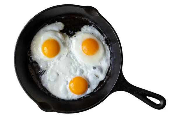 Three fried eggs in cast iron frying pan isolated on white from — Stock Photo, Image