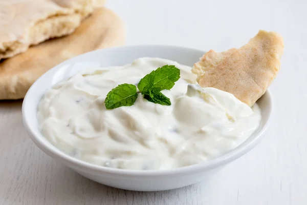 Tzatziki in white ceramic bowl with mint leaf garnish and a piec — Stock Photo, Image