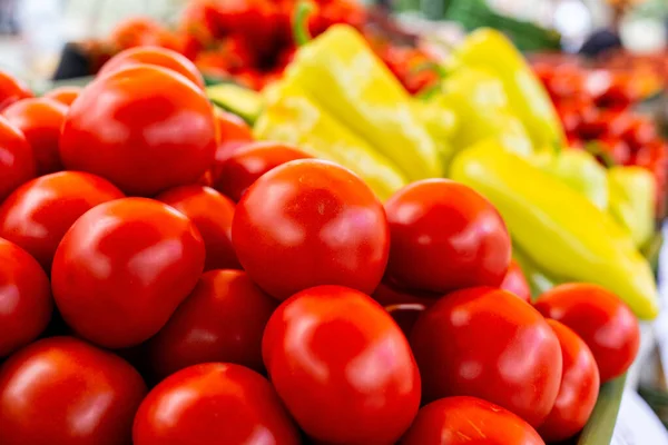 En hög med röda tomater på marknaden. Grönsaker i bakgrunden. — Stockfoto