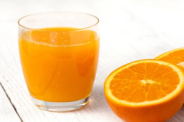 Glas orrange sap naast gehalveerd sinaasappel. Witte hout backgro — Stockfoto