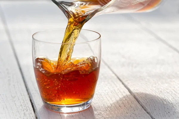 Pouring ice tea from a glass jug into a glass. White wood backgr — Stock Photo, Image