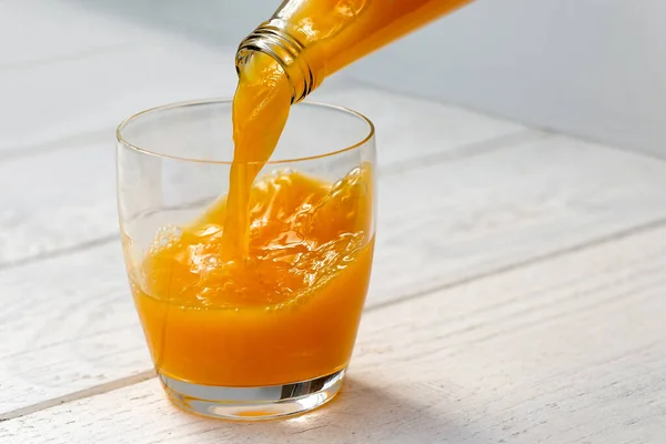 Sinaasappelsap uit een glazen fles in een glas gieten. Witte woo — Stockfoto