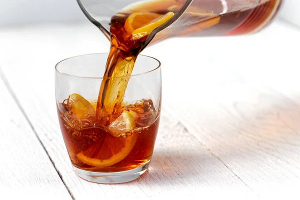 Pouring ice tea with lemons from a glass jug into a glass. White — Stock Photo, Image