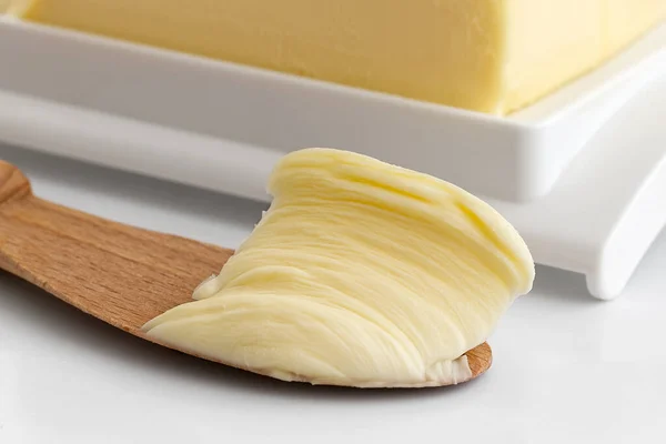 Detalle de mantequilla untada en un cuchillo de madera junto a una mantequilla de plástico —  Fotos de Stock