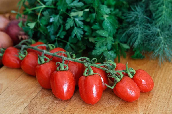 Grape tomatoes on vine  on wood chopping board in front of a bun — Stock Photo, Image