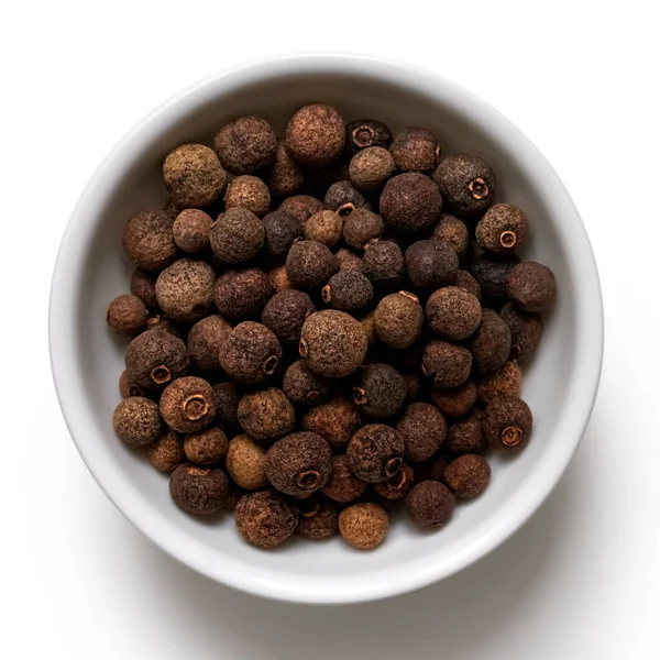 Whole allspice in white ceramic bowl isolated on white from abov — Stock fotografie