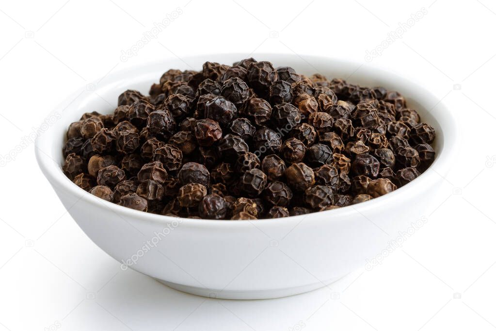 Whole black peppercorns in white ceramic bowl isolated on white.