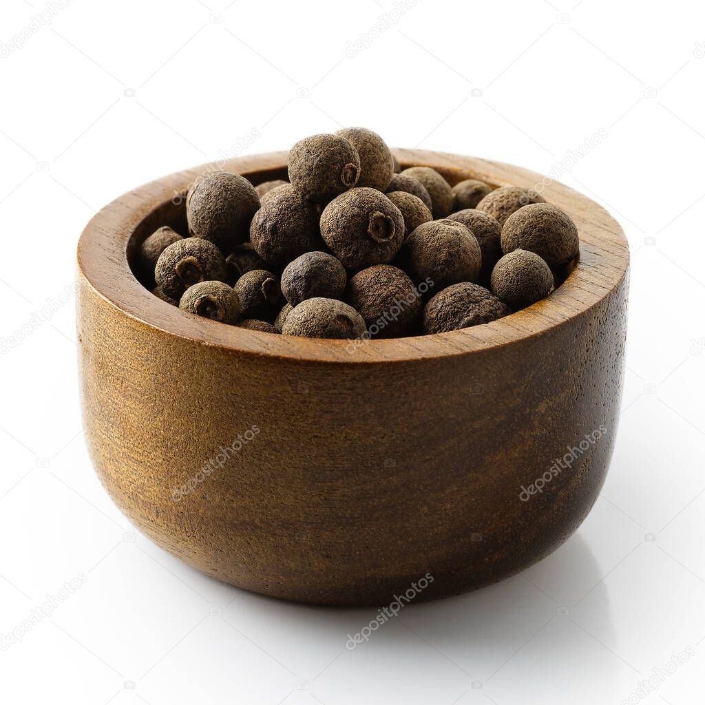 Whole allspice in dark wood bowl isolated on white.