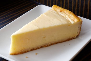 Beyaz seramik tabakta bir dilim fırında peynirli kek. Koyu b