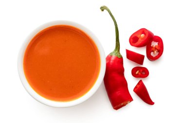 Peri peri acı biber sosu beyaz bir seramik kasede, dilimlenmiş bir tabağın yanında. 