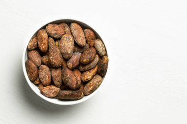 Kavrulmuş kabuksuz kakao çekirdeği beyaz seramik bir kasede izole edilmiş.