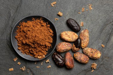 Kavrulmuş kabuğun yanında siyah seramik bir tabakta kakao tozu. 
