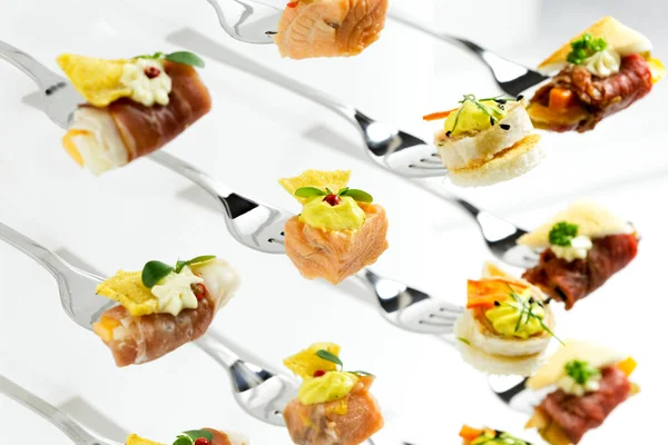 Background of mixed canapes on metal forks. White background. — ストック写真