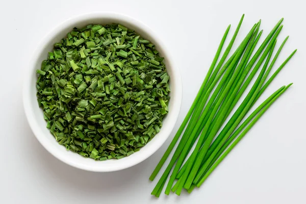 Dried chopped chives in white ceramic bowl next to a pile of who — Stock Photo, Image