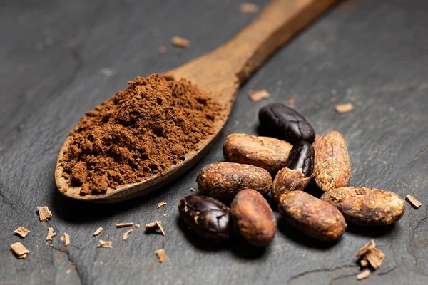 Cacao in polvere su un cucchiaio di legno accanto a pelato arrosto e sbucciato — Foto Stock